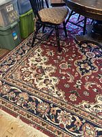 Full view of the red wool area rug under a dining table with floral patterns and fringed edges.