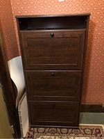 Full view of the wooden shoe rack cabinet from the front, showing the three drop-down doors and the open top shelf with its dark brown finish.