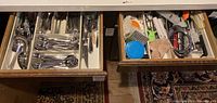 Two open drawers showing organized stainless steel silverware and assorted kitchen utensils including graters and peelers.
