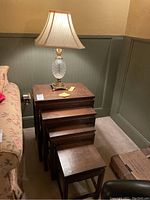 Perspective showing full set of four wooden nesting tables stacked together beside a sofa and the crystal lamp placed on top.