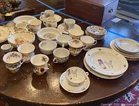 Photo showing an array of Royal Doulton Bunnykins cups, saucers, and bowls arranged on a wooden round table.