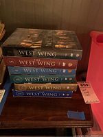 Stacked DVD box sets of The West Wing seasons 1 through 5, each spine visible with season number and title.