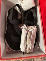 Black Skechers sandals with elastic straps inside red box with tissue paper