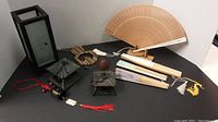 Overview photo showing all decorative Asian-themed items including two folding fans, wooden fan, lantern lantern-style candle holder, pagoda-shaped candle holders, brass bell with red knot, and beige coil item.