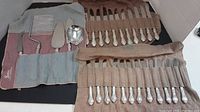 Two fabric roll-up cases opened showing 12 matching forks in one and 12 matching knives in the other alongside a smaller pouch of four serving tools.
