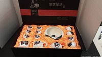 Full boxed set showing arrangement of teapot, tea cups, bowl, and cup with saucer on orange satin inside black box