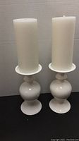 Pair of white ceramic candle holders each topped with a large white pillar candle, shown side by side to indicate the full lot contents.