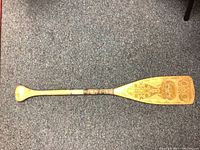 Full view of the canoe paddle showing one side with Indigenous art and wrapped handle section.