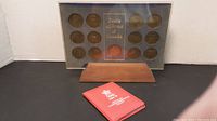 Frontal view of the Coats of Arms of Canada coin set with blue background and wooden stand, including the closed red case of the Calgary 88 silver ingot