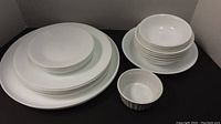 White Corelle dishes stacked by size including dinner plates, side plates, medium and small bowls.