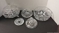 Overall view of five cut crystal serveware pieces including two large bowls (one with lid and feet), butter dish with lid, ashtray, and a small dish.