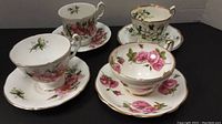 Four cups and matching saucers with floral designs and gold trim, arranged in pairs.