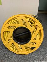 Front view of yellow electrical cord tightly wound on circular yellow reel with black handle in center.