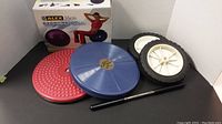 Set of items including two ab twisters, purple exercise ball in box, and roller wheels with handle bar all arranged on floor against a white background.