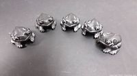 Five pearlite Stonecraft frog figurines arranged in different formations on a black surface, showing details and size.