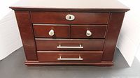 Front view of closed large wooden jewelry box with multiple drawers and silver-tone handles
