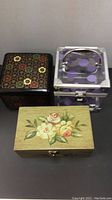 Front view of three jewelry boxes including wood lacquer floral box, black lacquer floral box, and clear purple polka-dot Caboodles box