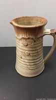 Photo showing side view of the pottery vase with handle, highlighting the brown drip glaze and floral decorations on beige background.