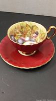 Front view of tea cup seated on saucer showing fruit motif and burgundy glaze