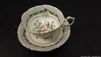 Tea cup sitting inside matching saucer, showing front floral and royal insignia decoration