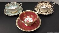 Three tea cup and saucer sets (mint green, cobalt blue, burgundy red) arranged front view