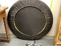 Front view of mini trampoline showing black padded edge and three detachable metal legs on floor.