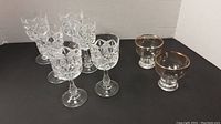 Photo showing set of six vintage cut crystal wine glasses and two smaller gold banded glasses on a black surface with white background.