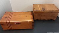Two wood jewelry boxes shown side by side on a black and white background; one cedar with latch, one natural wood grain