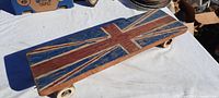Top side view of handmade solid wood skateboard featuring hand-painted British flag (Union Jack) design, showing worn paint and wood texture.
