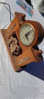 Side angle view of the antique wooden clock showcasing the rounded wooden case, carved floral decorations, and finials.