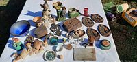 Wide view of all items laid on white cloth displaying assortment of figurines, plaques, ceramics, small collectible items with earth tone and colorful accents.