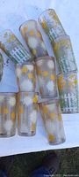 Photo showing 10 antique drinking glasses with colorful applied label designs, including yellow flowers with white picket fence and white/yellow sunburst patterns on frosted glass.