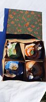 Top view of four ceramic flower-shaped dishes with attached animal figurines in original printed box.