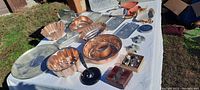 Various copper and aluminum pans and molds displayed on a white tablecloth outside with grass background.