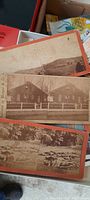 Photo showing a few of the stereo cards with orange borders and old sepia-tone images including rural houses and a fence.