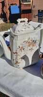 White porcelain or glass teapot with rectangular body, floral gold trim, decorative handle and lid.