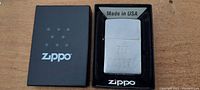 Photo of vintage Zippo lighter in original black box showing the Zippo logo on the box and the lighter face with '717 TATTOO' inscription.
