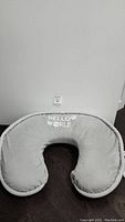 Gray Boppy Luxe nursing pillow with "Hello World" embroidered on top and matching gray piping, lying on a dark floor, photographed from above.