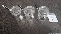 Front angle shot of three clear chutney jars with lids and spoons on a dark surface.