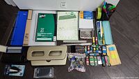 Overview of all desktop office supplies spread on floor including binders, notebooks, pens, organizers, staplers, hole punchers, letters opener, paper clips, sticky notes and labels.