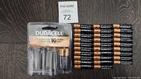Photo showing one pack labeled Duracell C4 containing one battery and 29 loose Duracell AAA batteries arranged in rows on wooden surface.