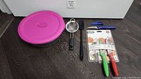 Full view of the kitchen utensils lot showing all items including Pyrex bowl with lid, silicone spatula, mini strainer, and Zyliss knives in packaging with covers.