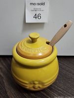 Yellow Le Creuset honey pot with lid and wooden handled honey dipper inserted into lid slot.