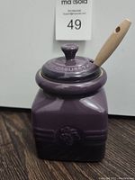 Front and side view of purple Le Creuset jam jar with lid and wooden handled spreader.