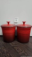 Frontal shot of two matching Le Creuset stoneware canisters with lids, showing height and embossed brand.