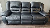 Front view of the black genuine leather power reclining sofa, showing three seat cushions and pillow top arms.