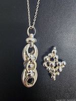 Close-up of two sterling silver pendants, one vertical with linked oval shapes and one bubble-like cluster pendant with rounded beads.
