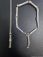 Close-up photo of the bamboo motif sterling silver pendant necklace alongside matching bamboo bracelet on black background.