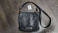 Front view of Marc By Marc Jacobs black leather crossbody purse showing metal logo plate and leather texture