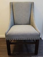 Front facing view showing grey upholstered seat and backrest with brass nailhead trim and wooden legs.